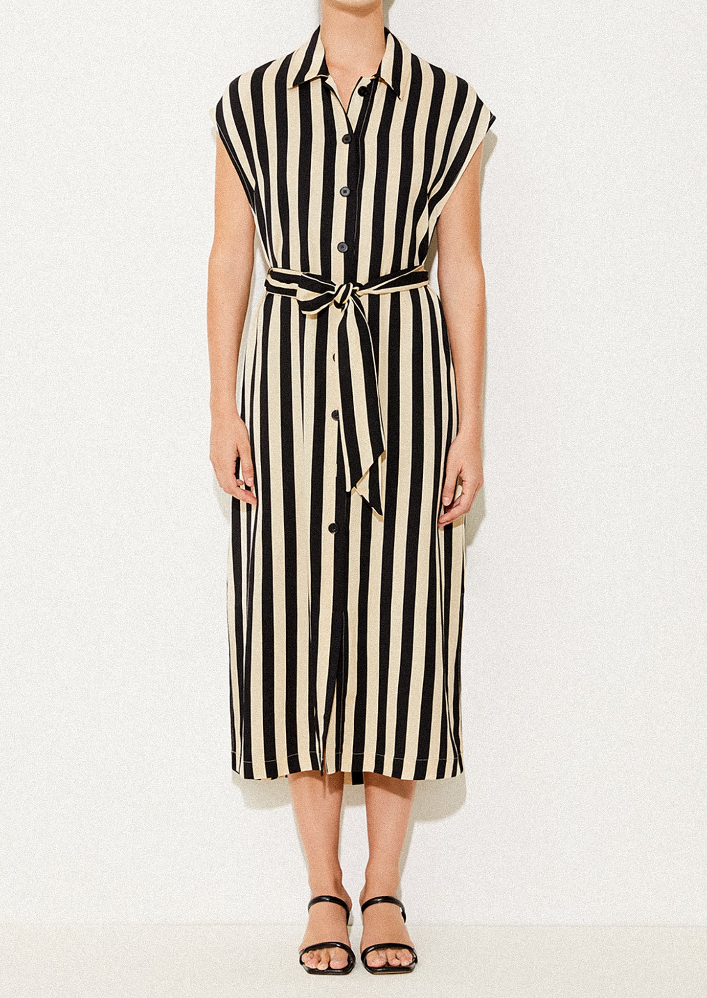 A woman wearing a sleeveless collared dress in vertical black and ivory stripes.