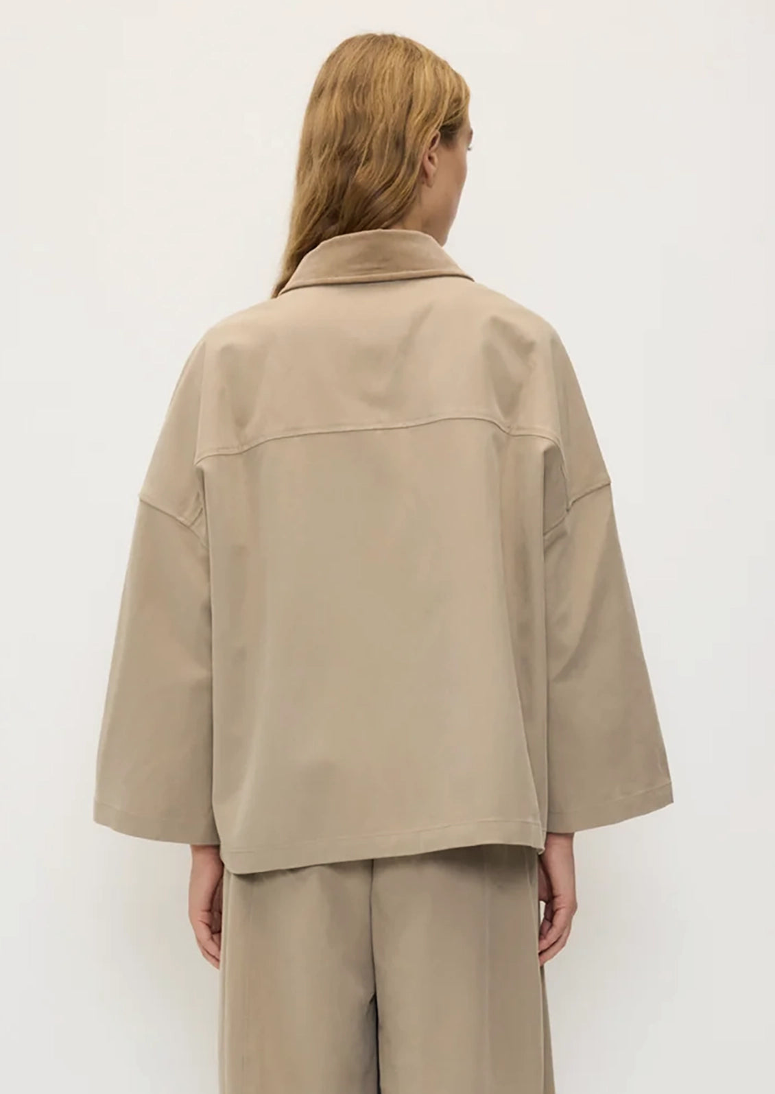 A person wearing a hip-length A-line jacket in khaki with tan contrast collar.
