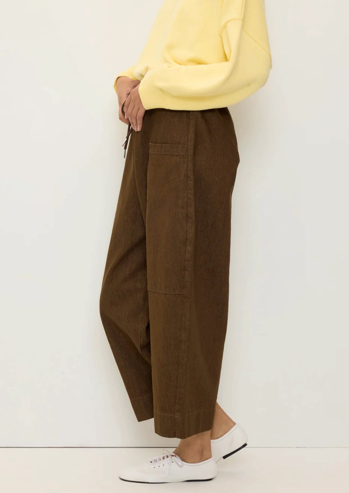 A person wearing a pair of brown denim pants with barrel leg shape and carpenter-style pockets.