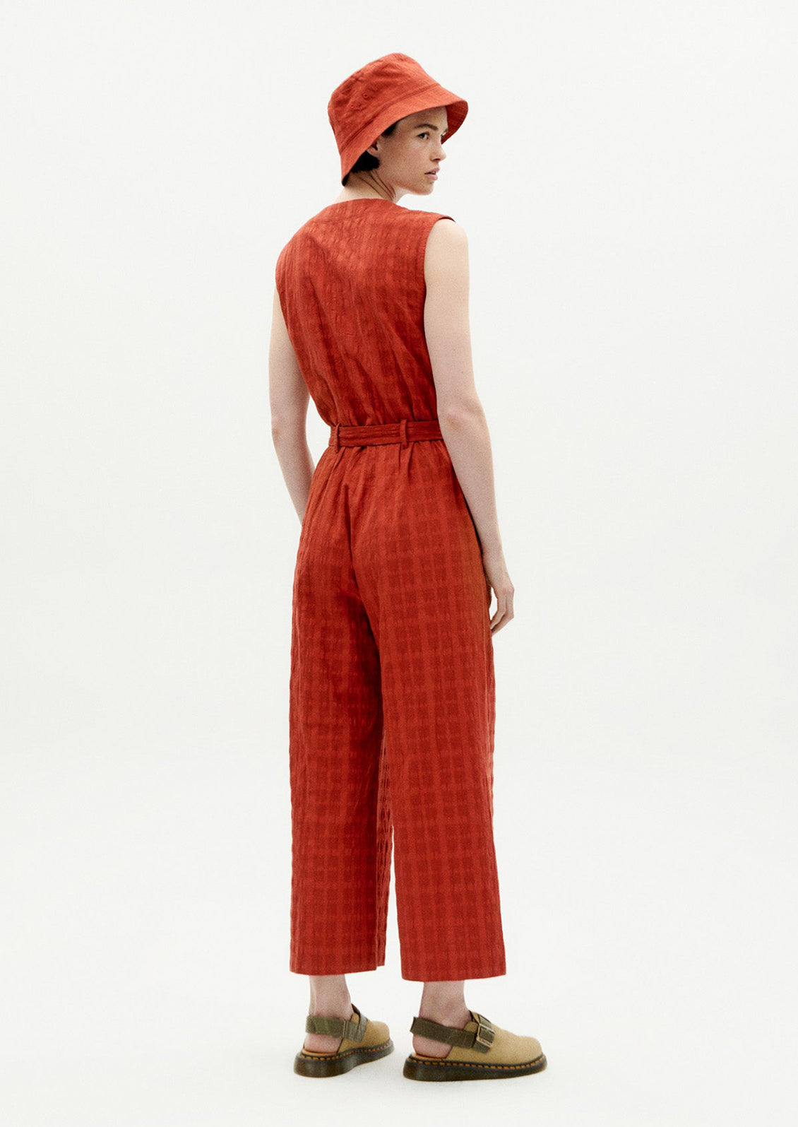 A woman wearing a rust colored jumpsuit with tie waist and tonal grid texture.