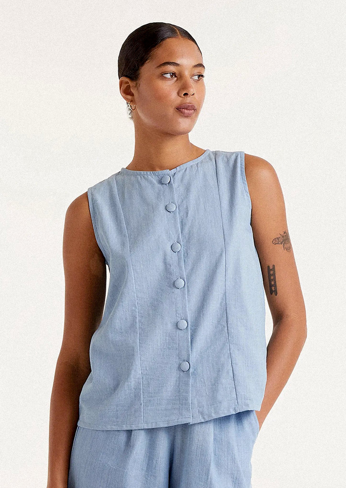 A person wearing a sleeveless round neck top with button front in blue chambray cotton.