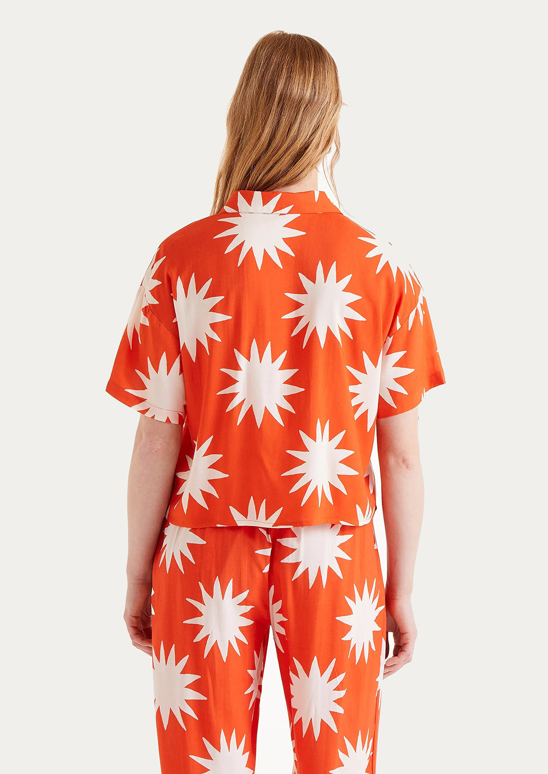 A short sleeve collared shirt in bright orange with big sun print in white.