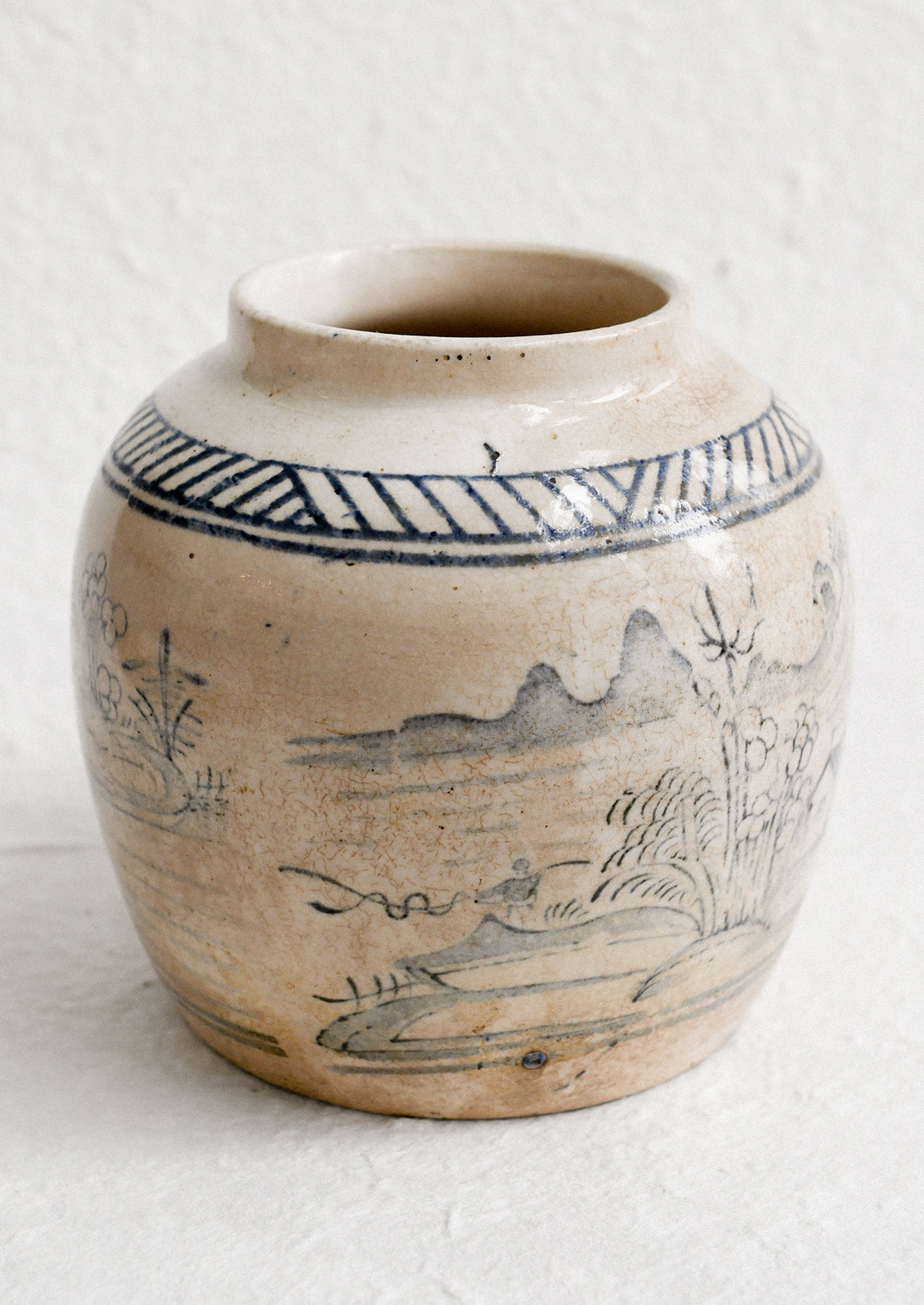 An aged stoneware ginger jar in beige patina with scenic scene in blue.