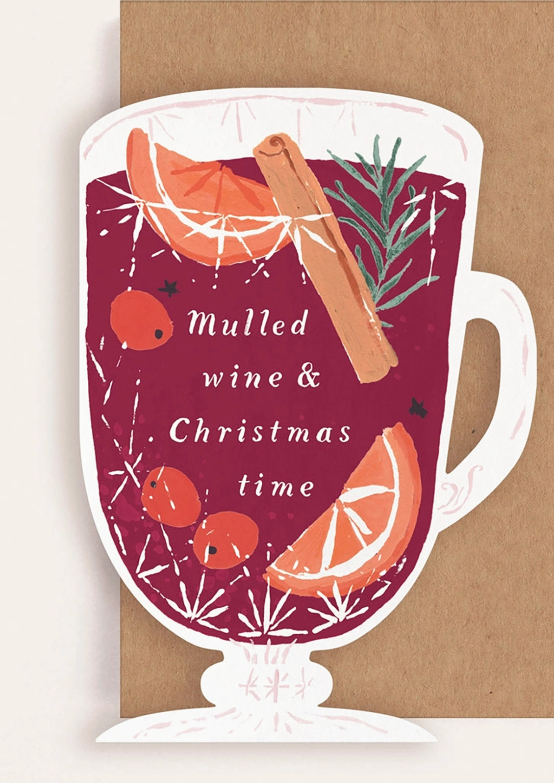 A festive illustrated card showing a white mug filled with deep red mulled wine, garnished with orange slices, a cinnamon stick, and a green sprig, with the text 'Mulled wine & Christmas time.' The design is photographed against a kraft brown background.