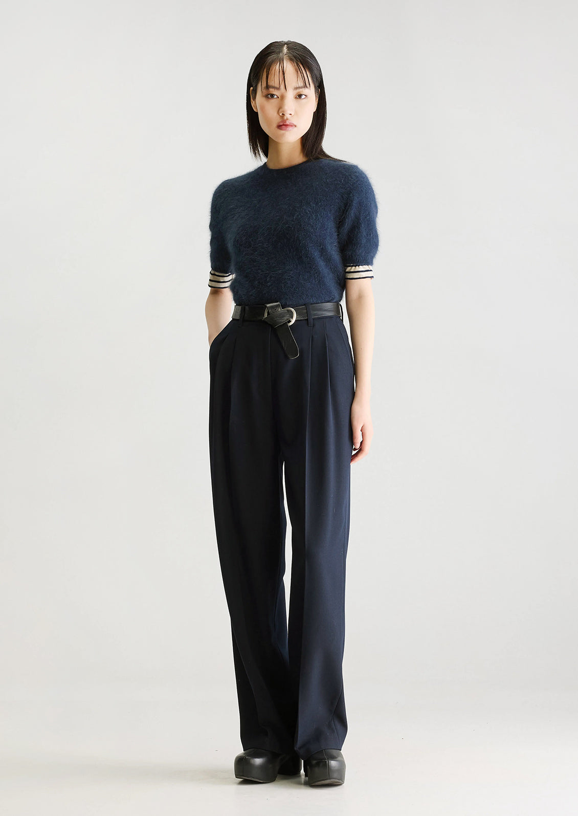 A person wearing a pair of navy blue dress trousers with pleated front.