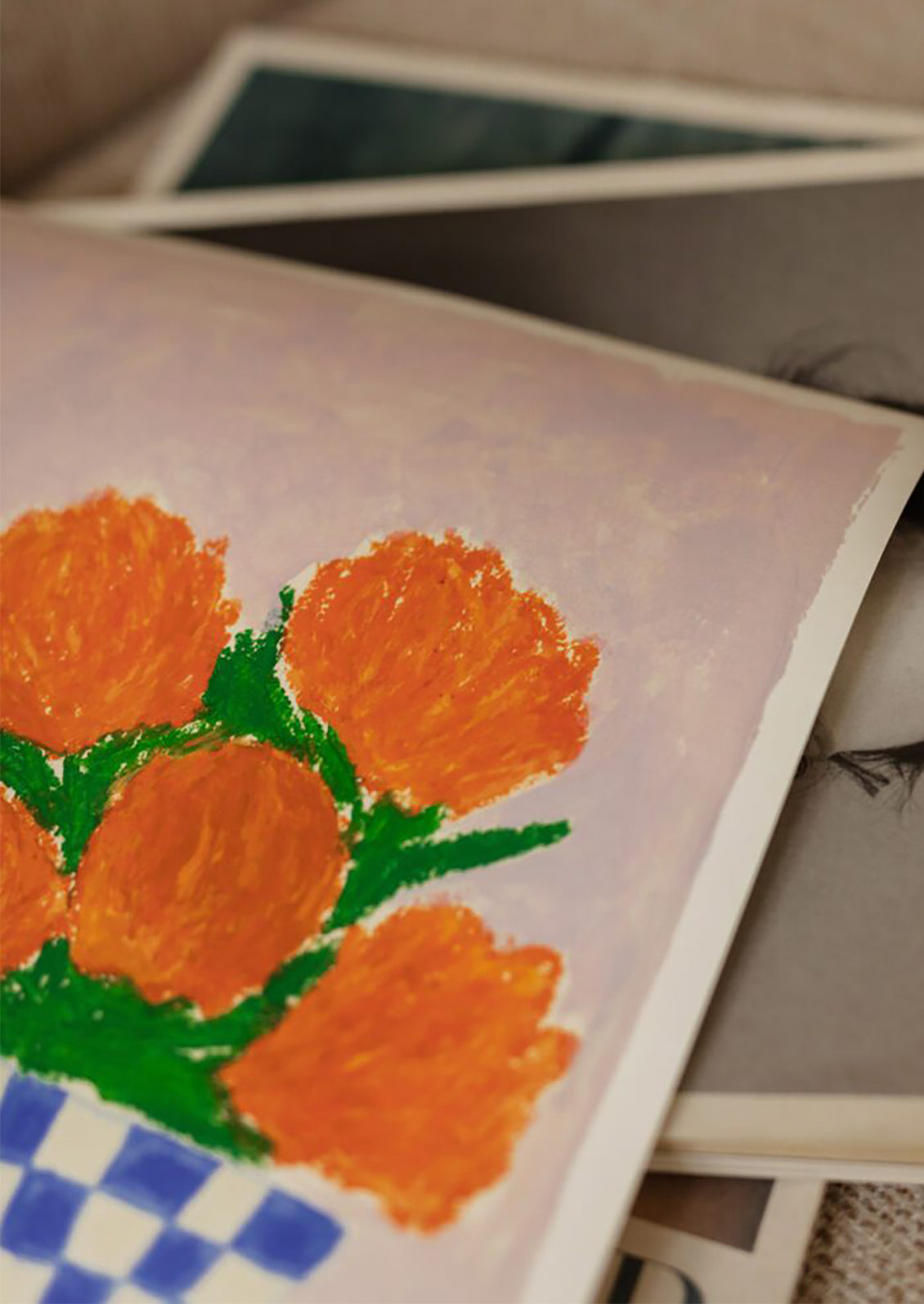 An art print of a painting of orange flowers in a blue and white checkered vase.
