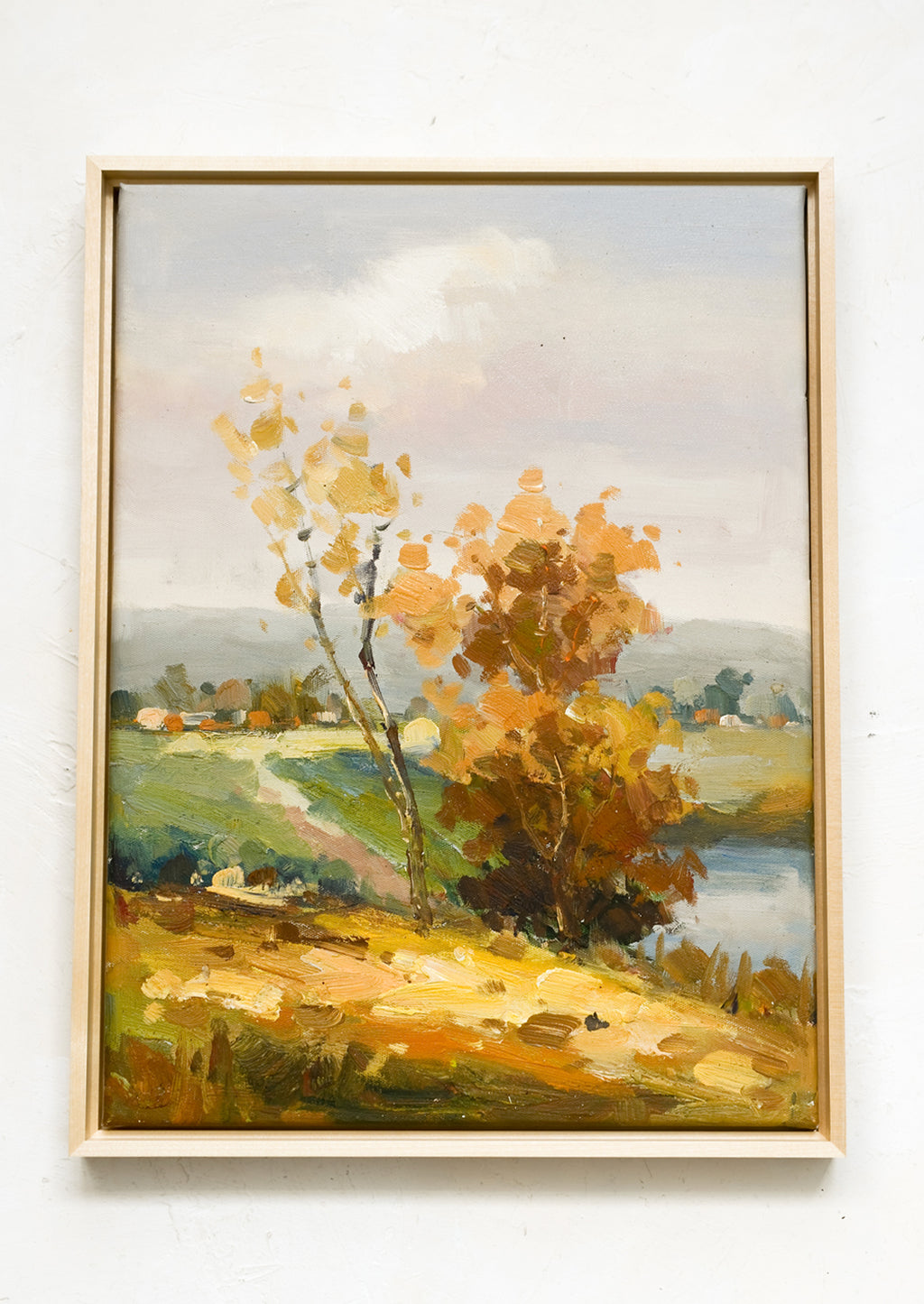1: A framed oil landscape painting of two trees next to a pond with houses in the distance.