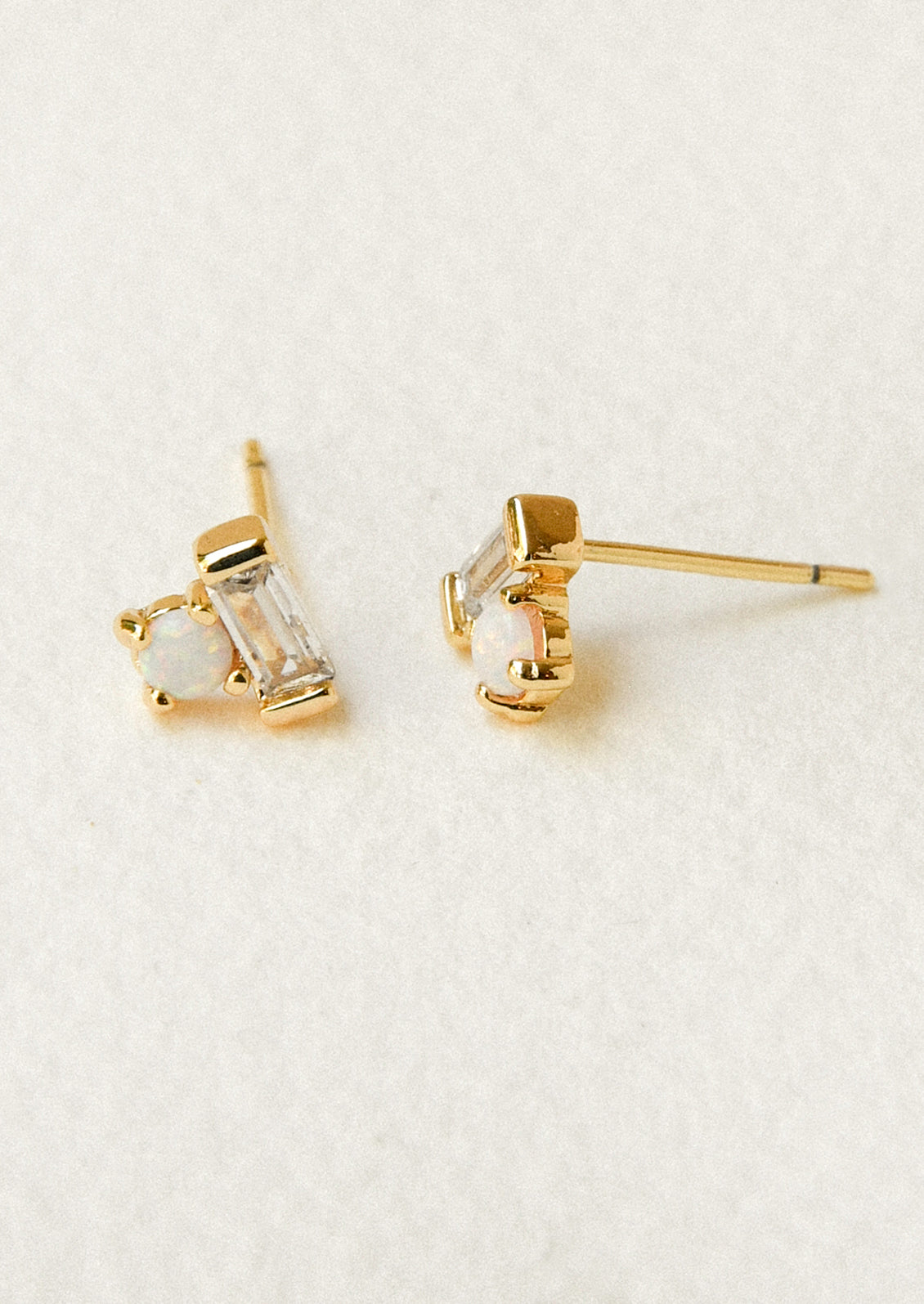 A pair of gold earrings with a baguette shaped gem stacked on top of an opal gem.