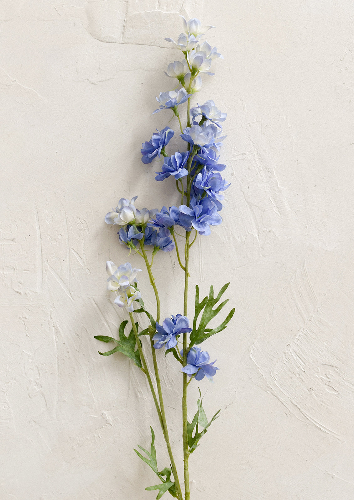 A faux flower stem depicting a periwinkle larkspur flower spray.
