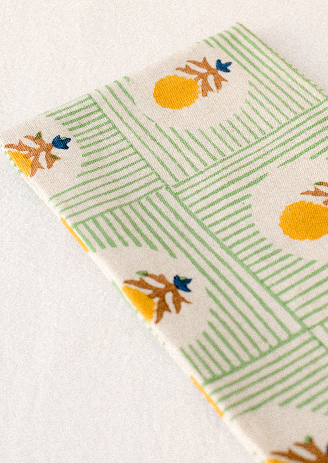 A block printed linen napkin in green stripe with yellow and brown floral.
