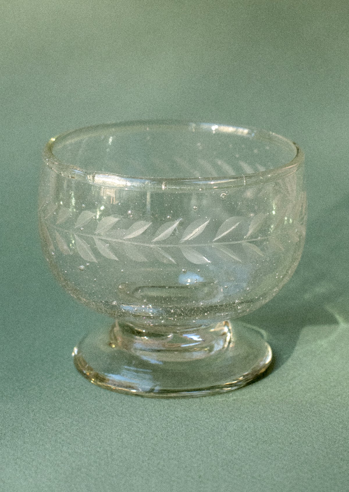 A stemmed cup in bubbled clear glass with etched laurel leaf pattern.