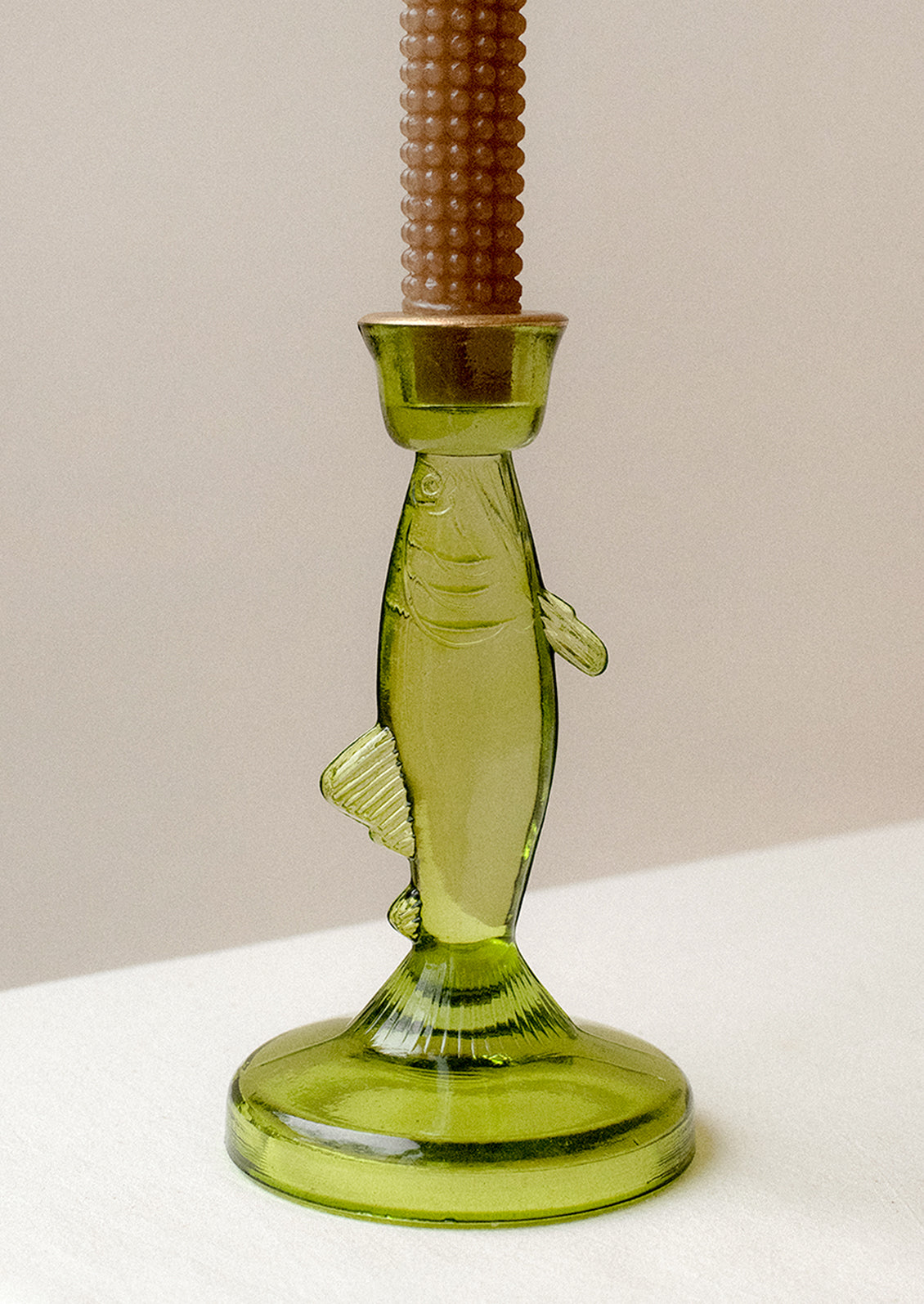 A green tinted translucent glass candle holder in the shape of a fish.