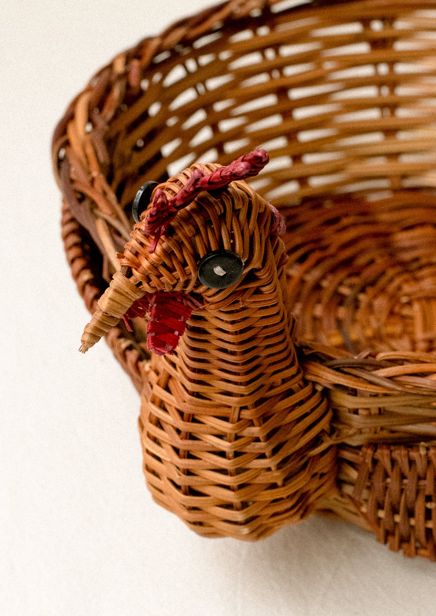 A woven basket with three dimensional chicken head detailing on side.