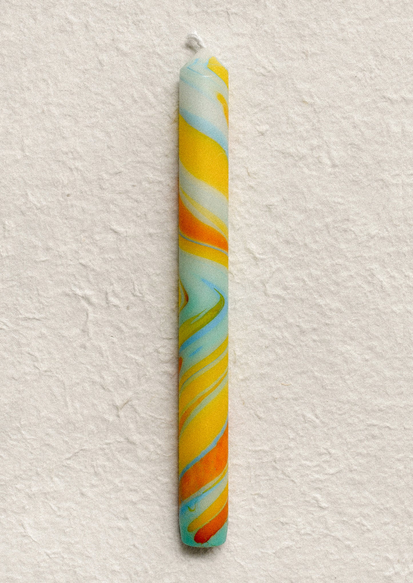 A marbled taper candle in blue, orange and yellow swirl pattern.
