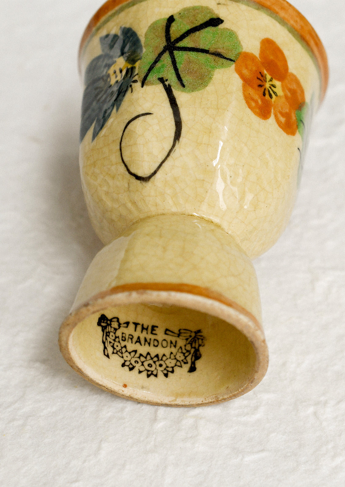 An antique egg cup in tan ceramic with caramel colored trim, and nasturtium floral pattern.