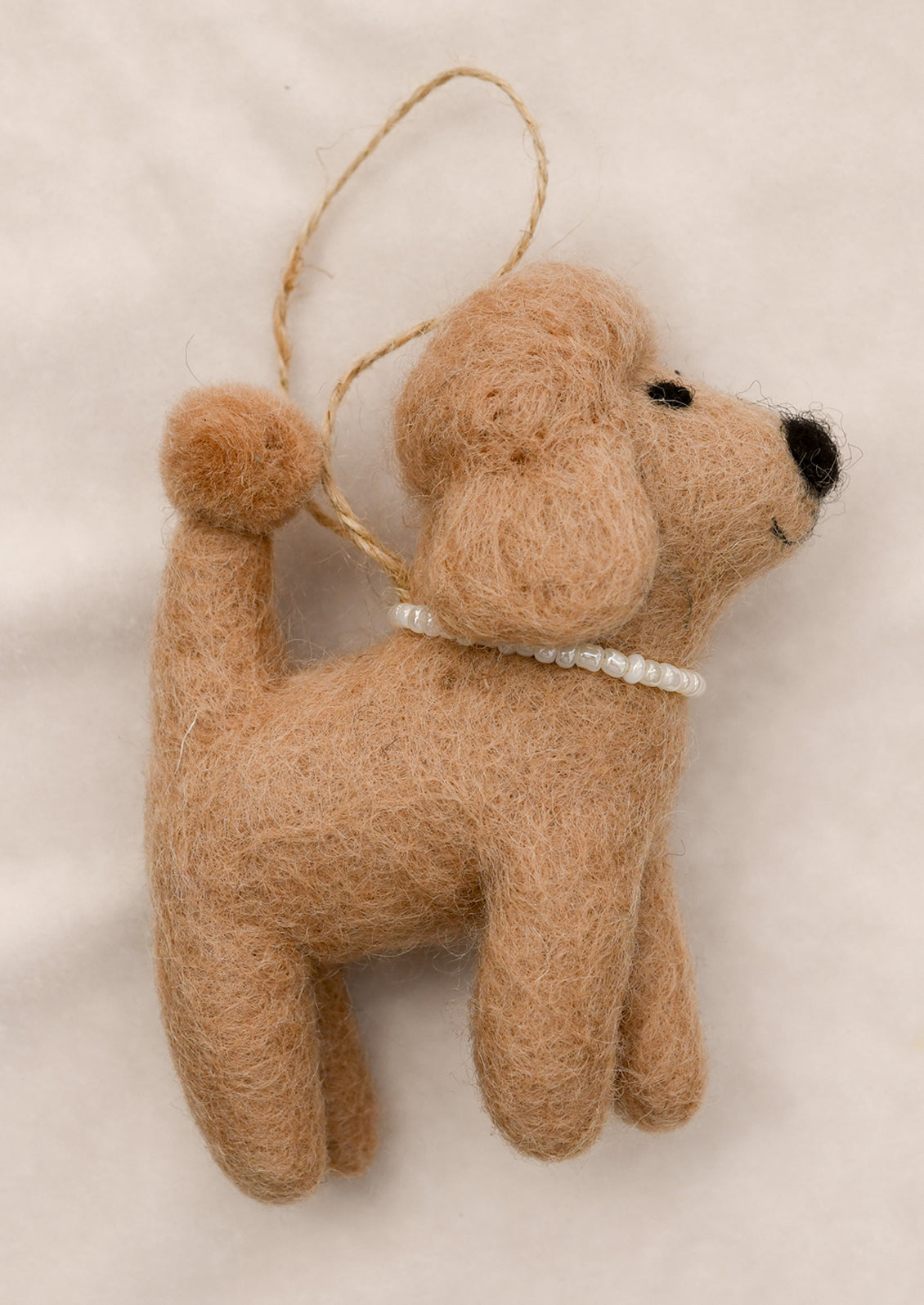 A felted ornament depicting a tan poodle wearing a pearl necklace.