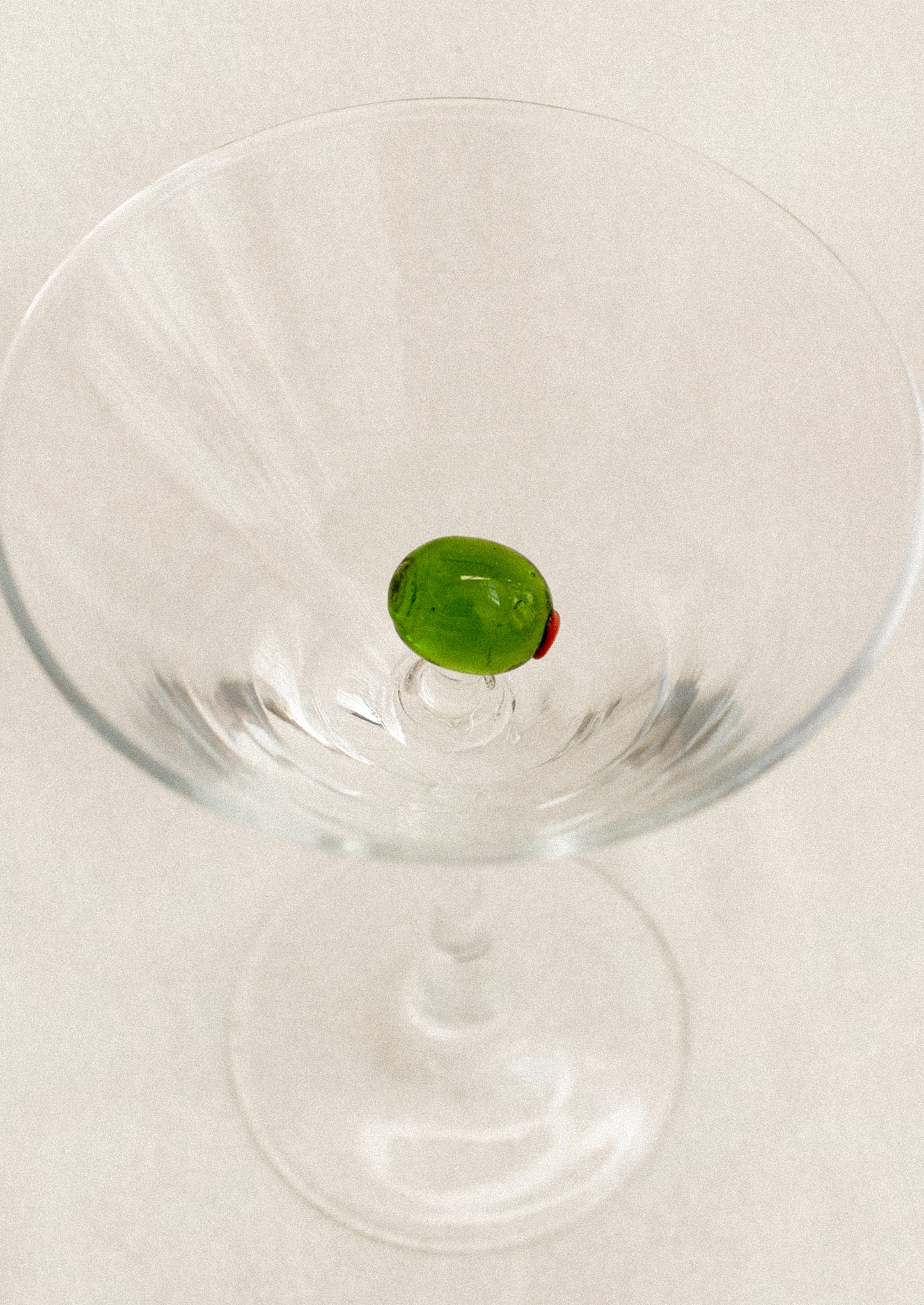 Clear martini glass with a glass olive decoration inside.