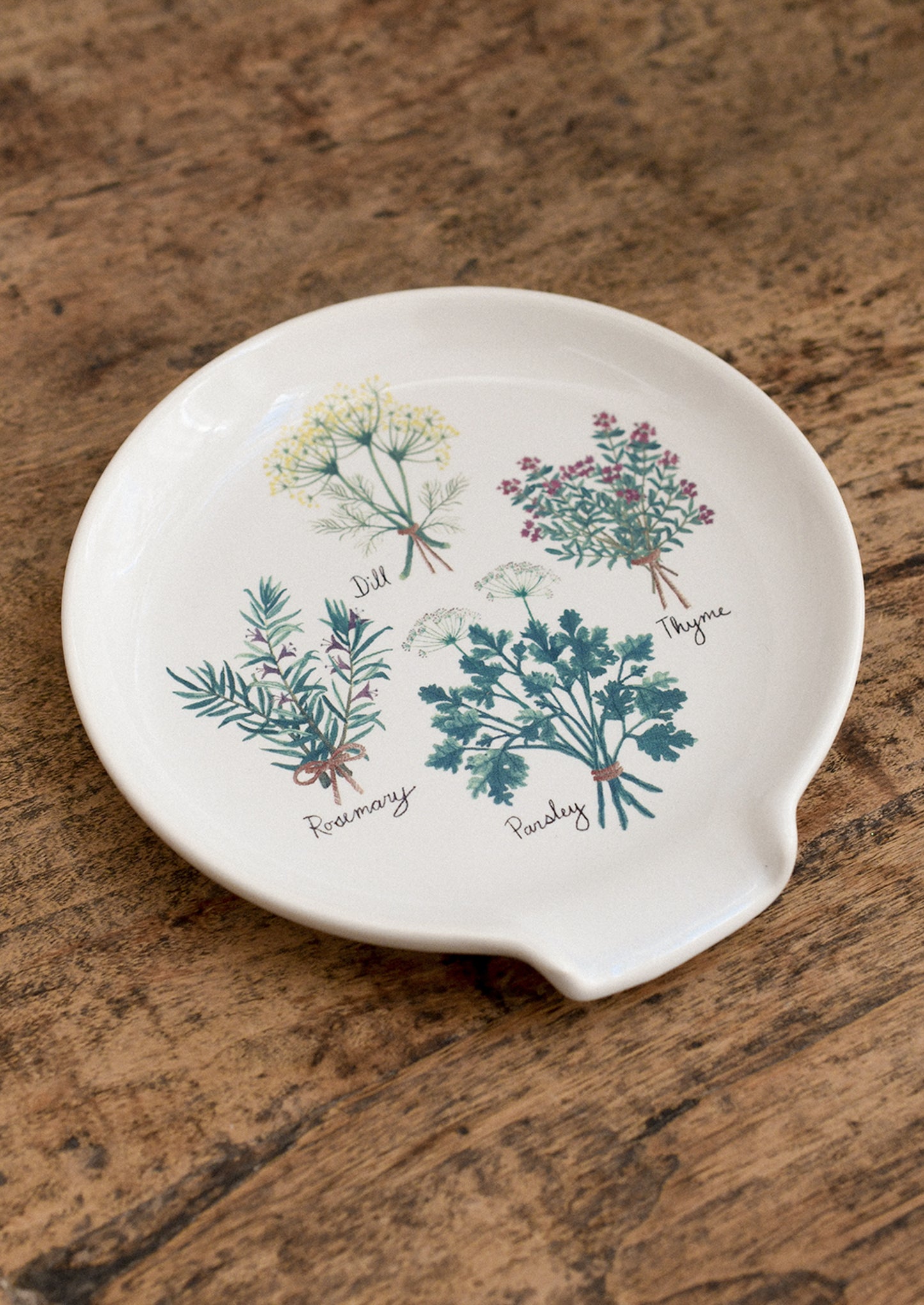 Decorative spoon rest with herb illustrations on a wooden surface