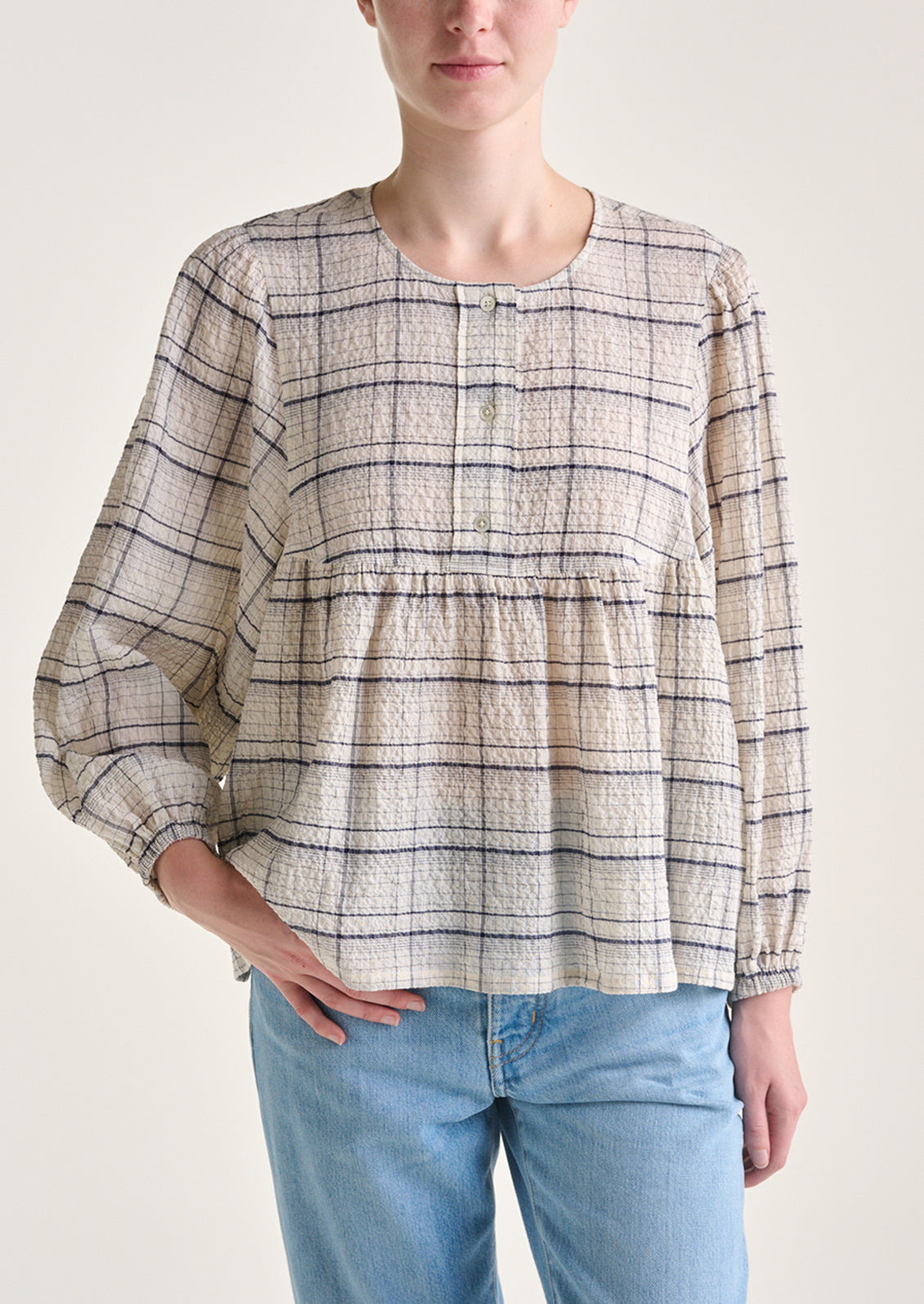 A woman wearing a crinkly textured blouse in ivory with navy check pattern.