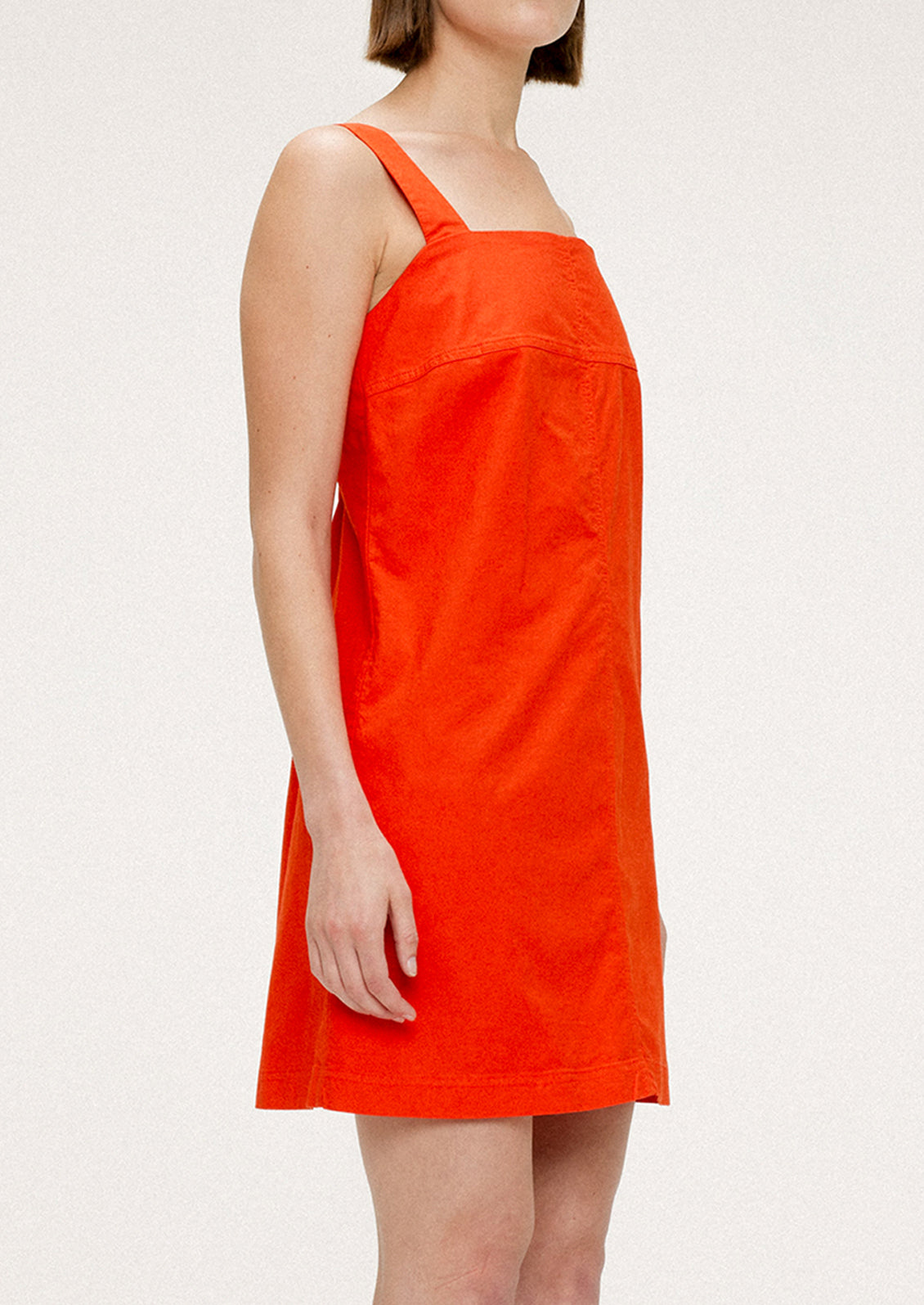 A woman wearing a short red-orange dress with square neckline and wide shoulder straps.