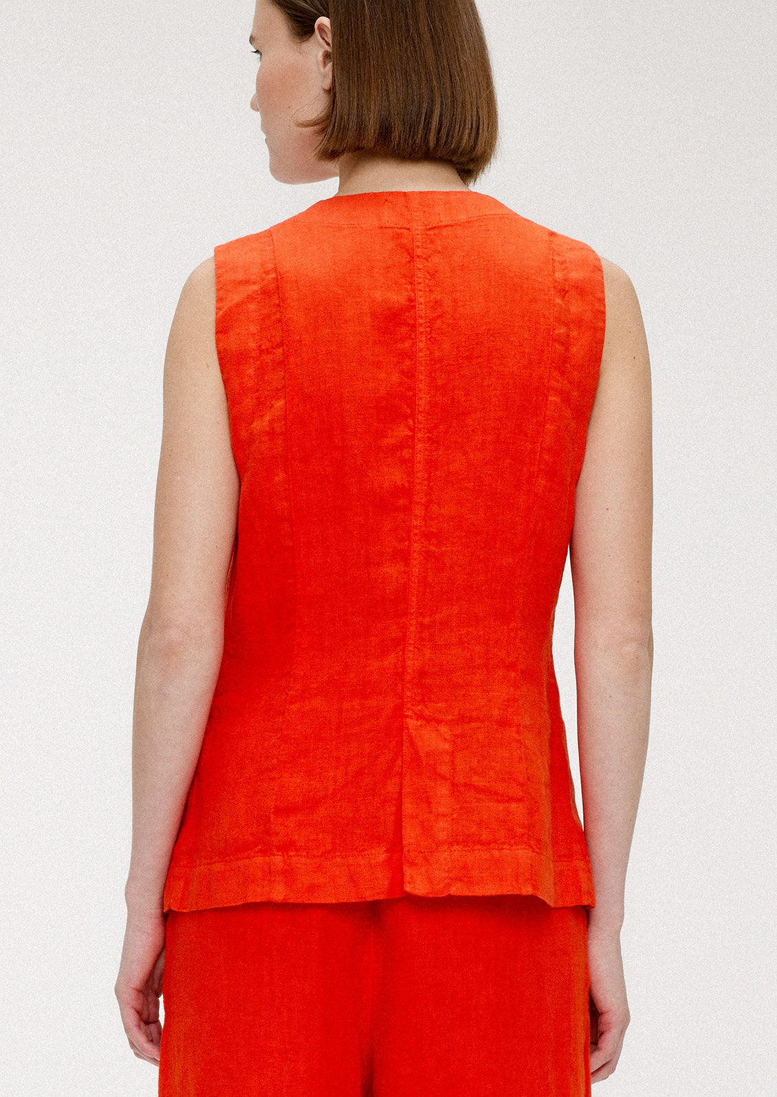 A woman wearing a sleeveless v-neck linen top in red orange hue.