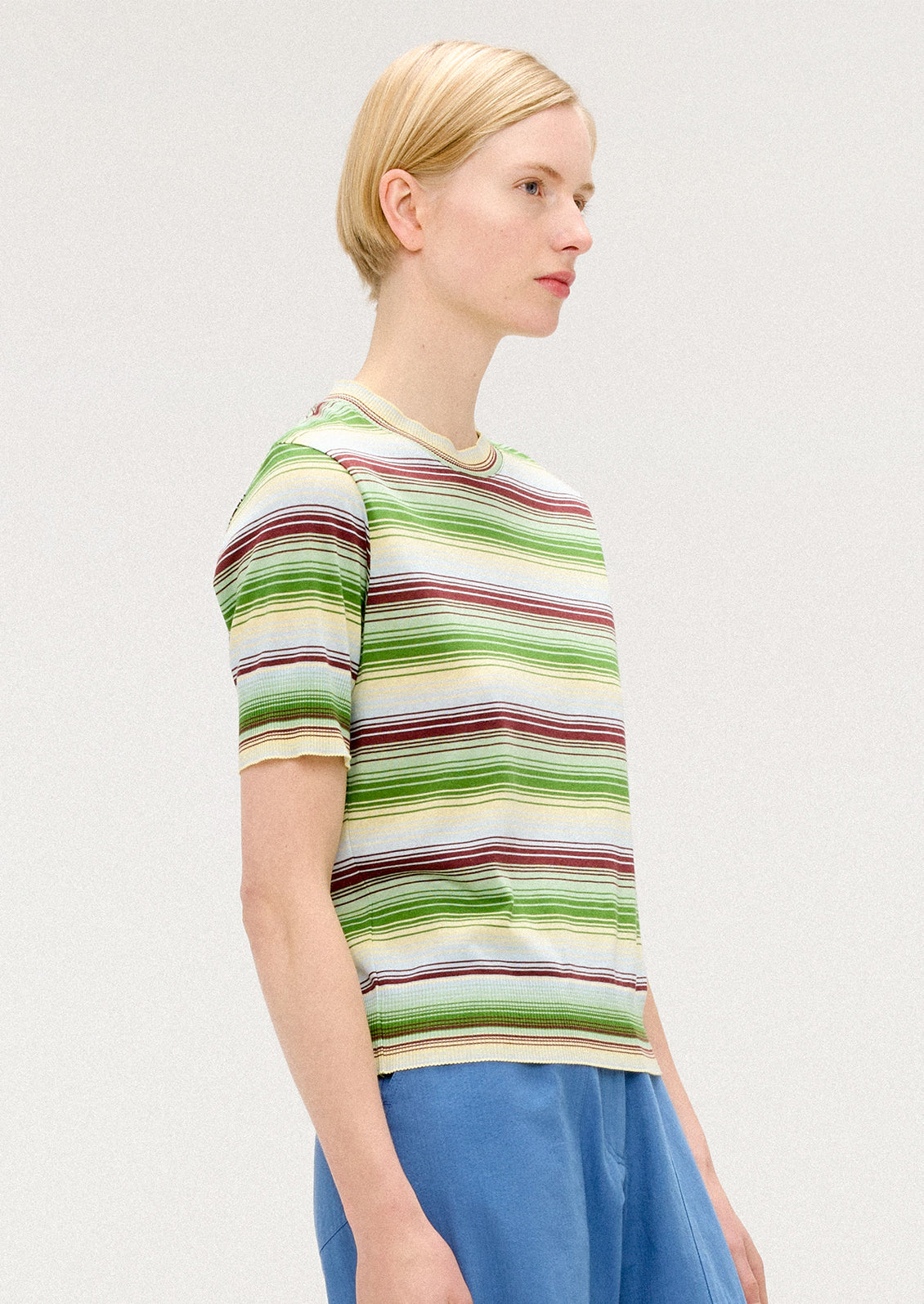 A person wearing a knit t-shirt with multi stripe pattern in green, cream and brown.