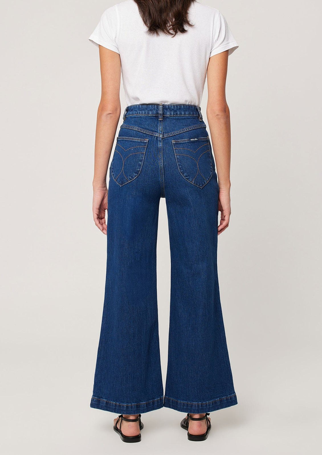 A woman wearing a pair of dark wash jeans with patch pockets at hips and wide leg shape.