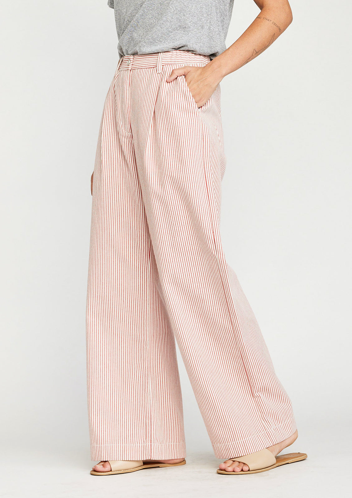 A woman wearing a pair of wide leg pleat front pants in red pinstripe.