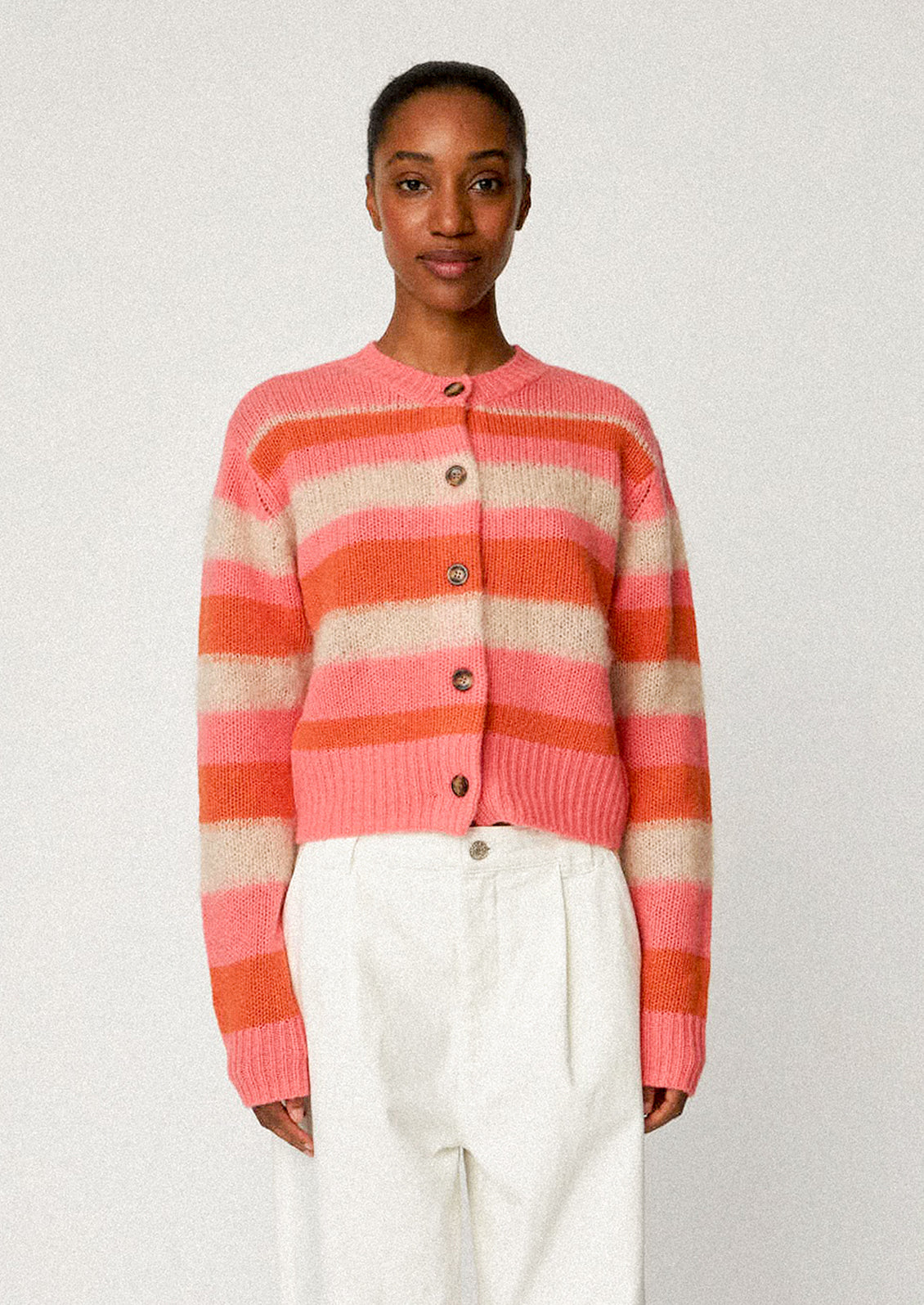 A woman wearing a button front cardigan sweater in pink, orange and ivory stripes.