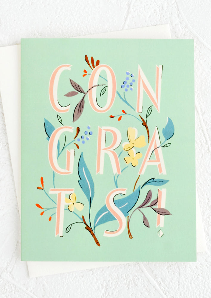 A mint colored greeting card with floral illustrated "CONGRATS" text.