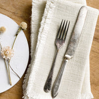 2: A pair of cream linen napkins with linen texture and fringed edges.