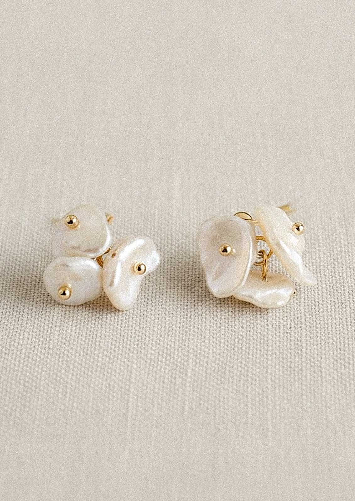 A pair of gold earrings with three freshwater pearls on each earring, set on a canvas fabric.