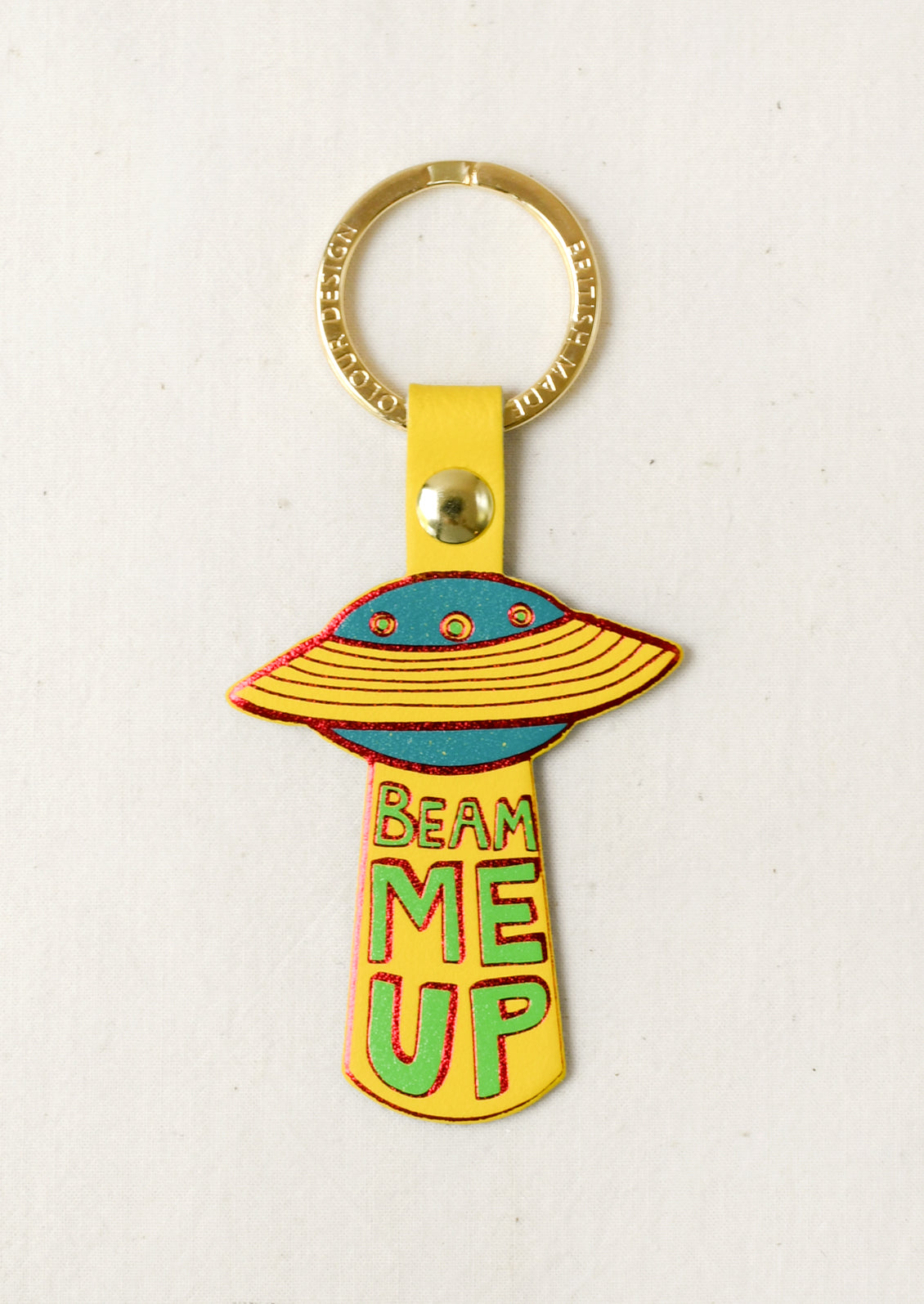 A leather keychain in the shape of a UFO with the words "Beam Me Up" on the front. Attached to a gold keyring.