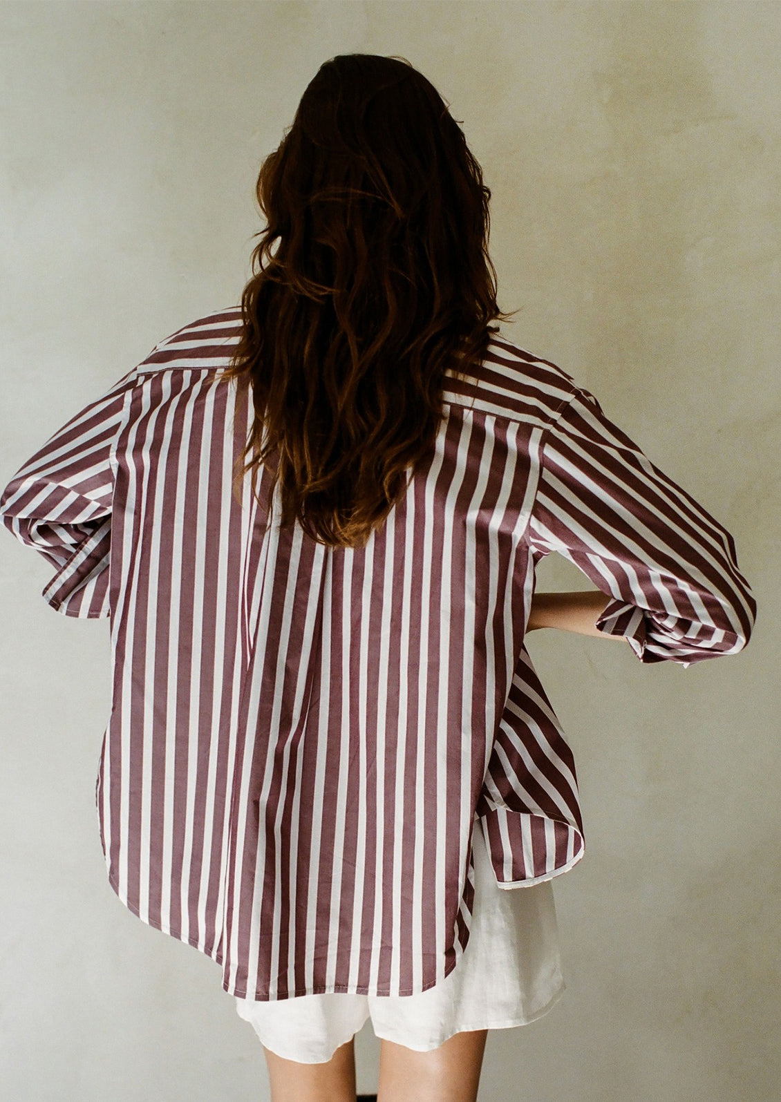 A woman wearing a tank and shorts with oversized striped button down shirt in burgundy and white.