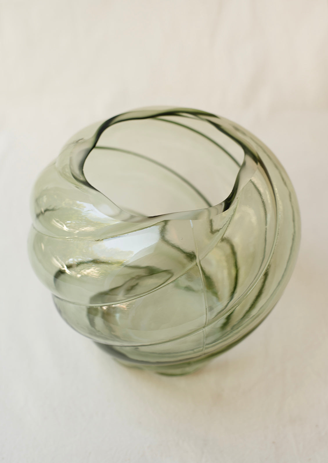 A glass vase in transparent olive green color, with twisted, tornado like texture.