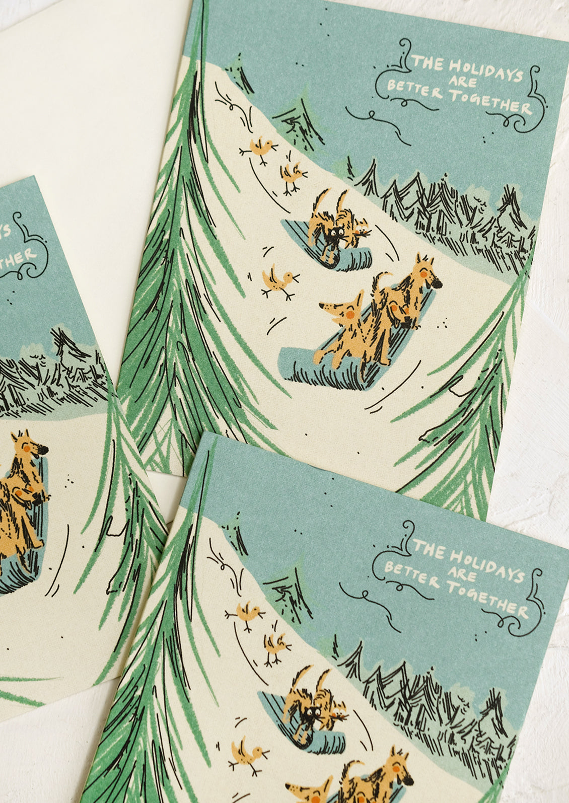 Greeting cards with illustration of dogs sledding down a hill, text reads "The Holidays Are Better Together".