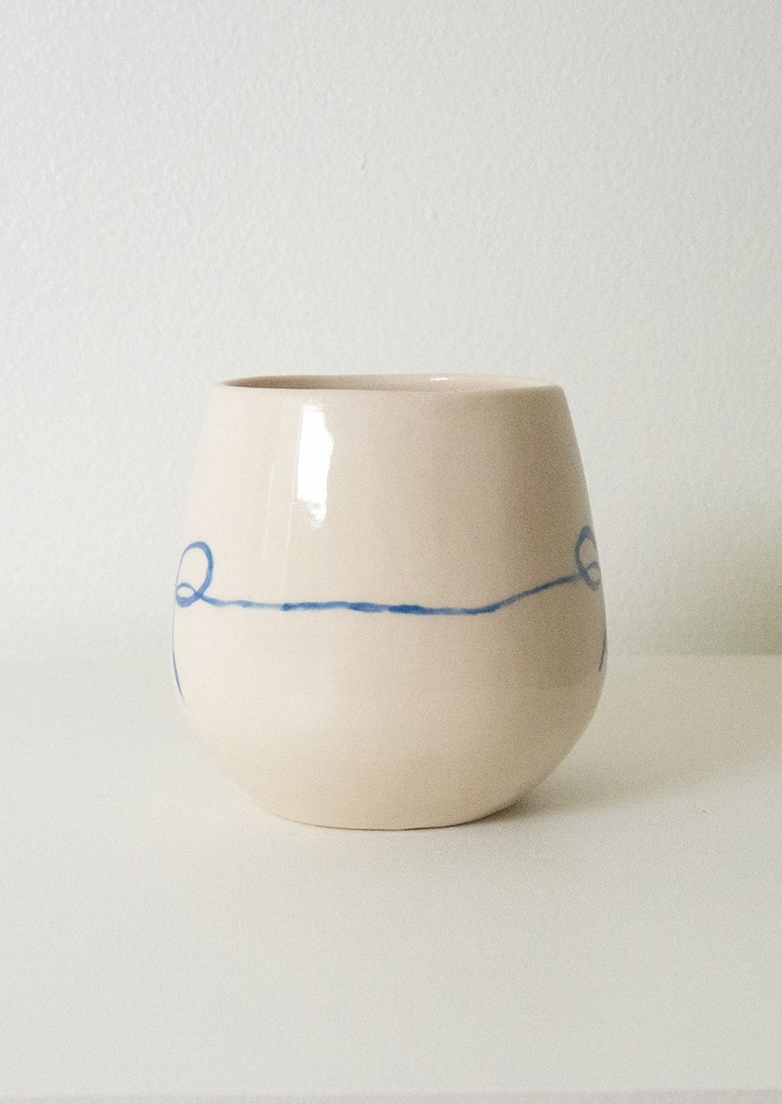 A white rounded ceramic cup with hand painted blue bow.