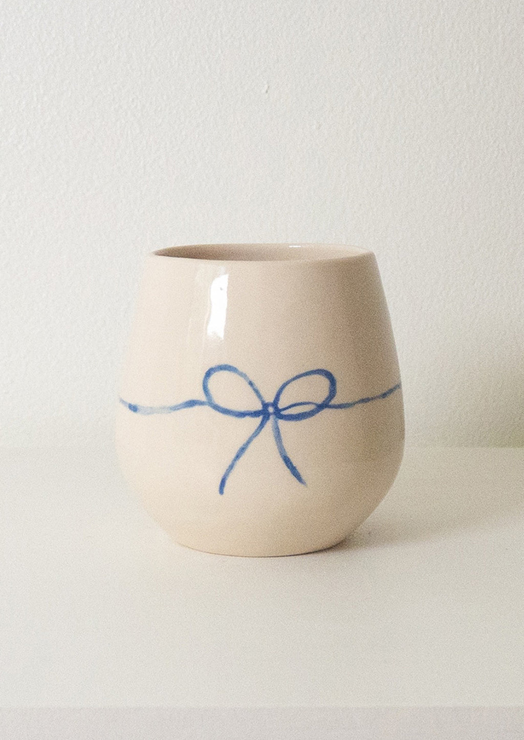 1: A white rounded ceramic cup with hand painted blue bow.