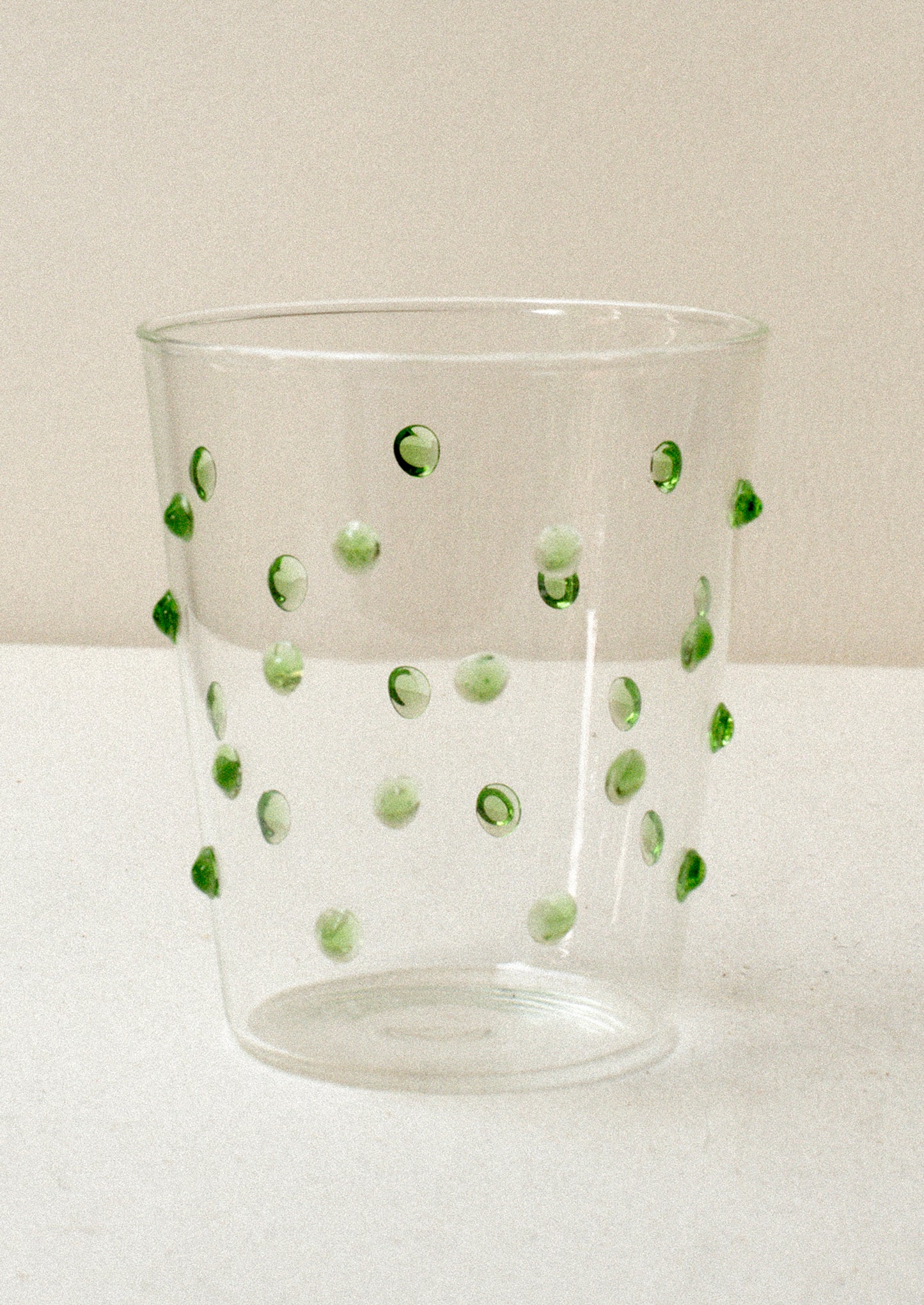 A clear glass tumblerswith textured raised dots on outside, in green.