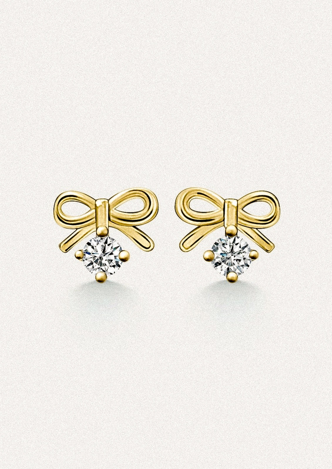 A pair of small gold stud earrings in the shape of a bow, with dangling cubic zirconia.