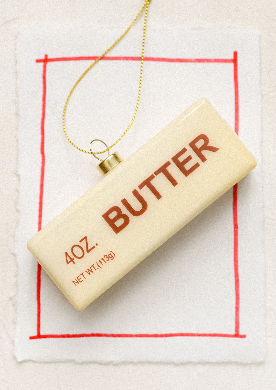A glass holiday ornament that looks realistically like a stick of butter in wrapper.