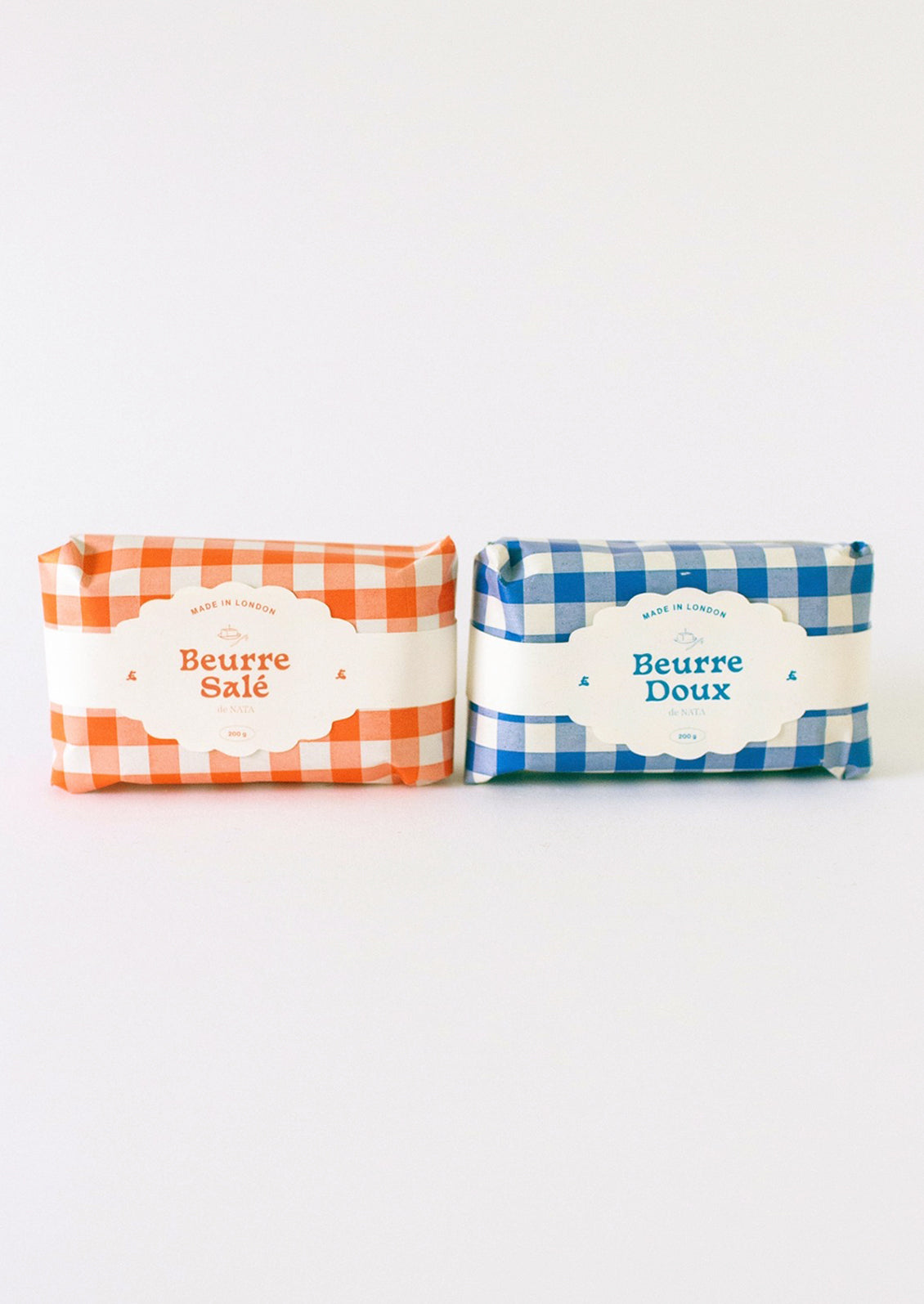 A candle in the shape of a block of butter, gingham packaging in red or blue.