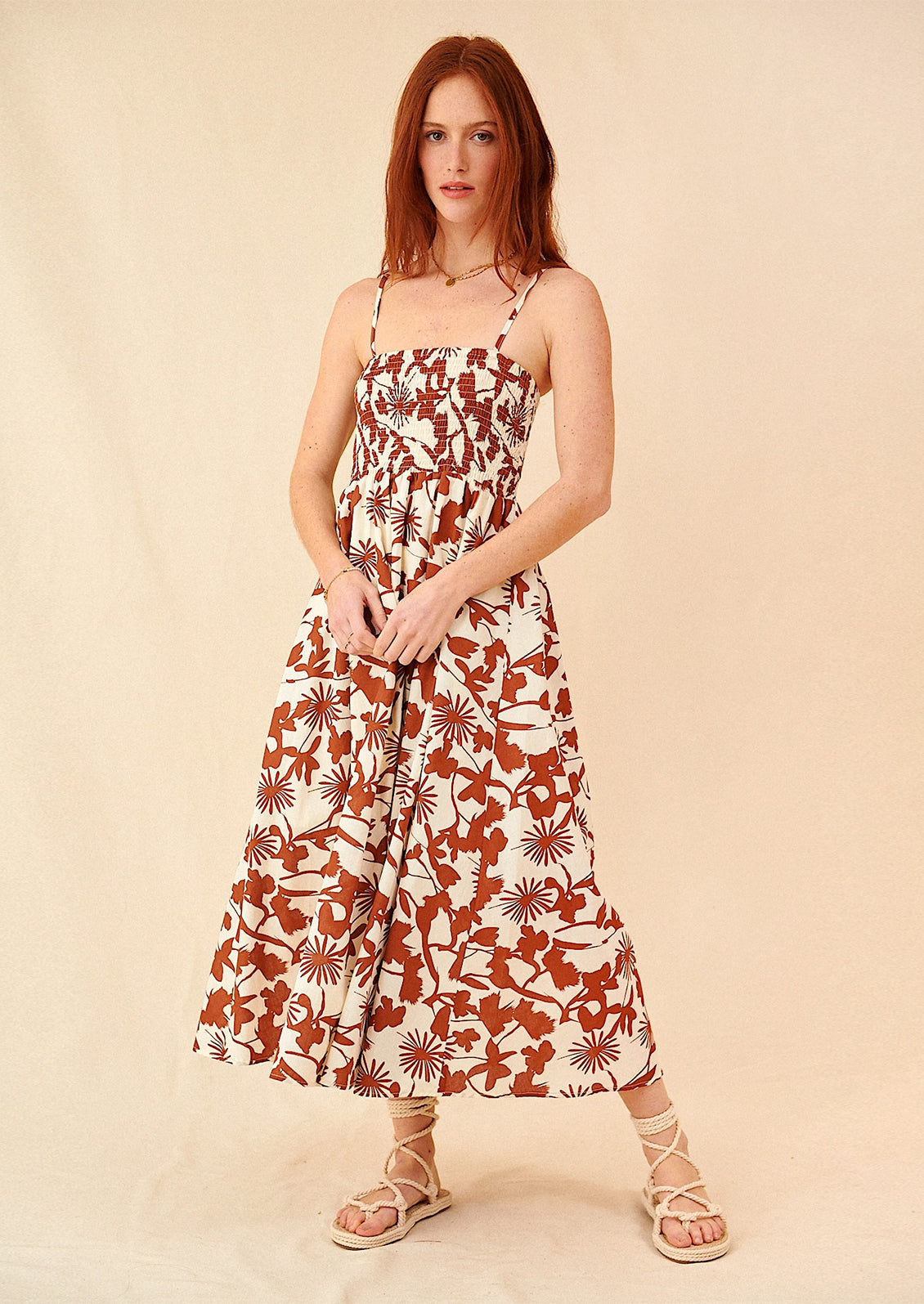 A woman wearing a sleeveless spaghetti strap dress in brown and white botanical print.