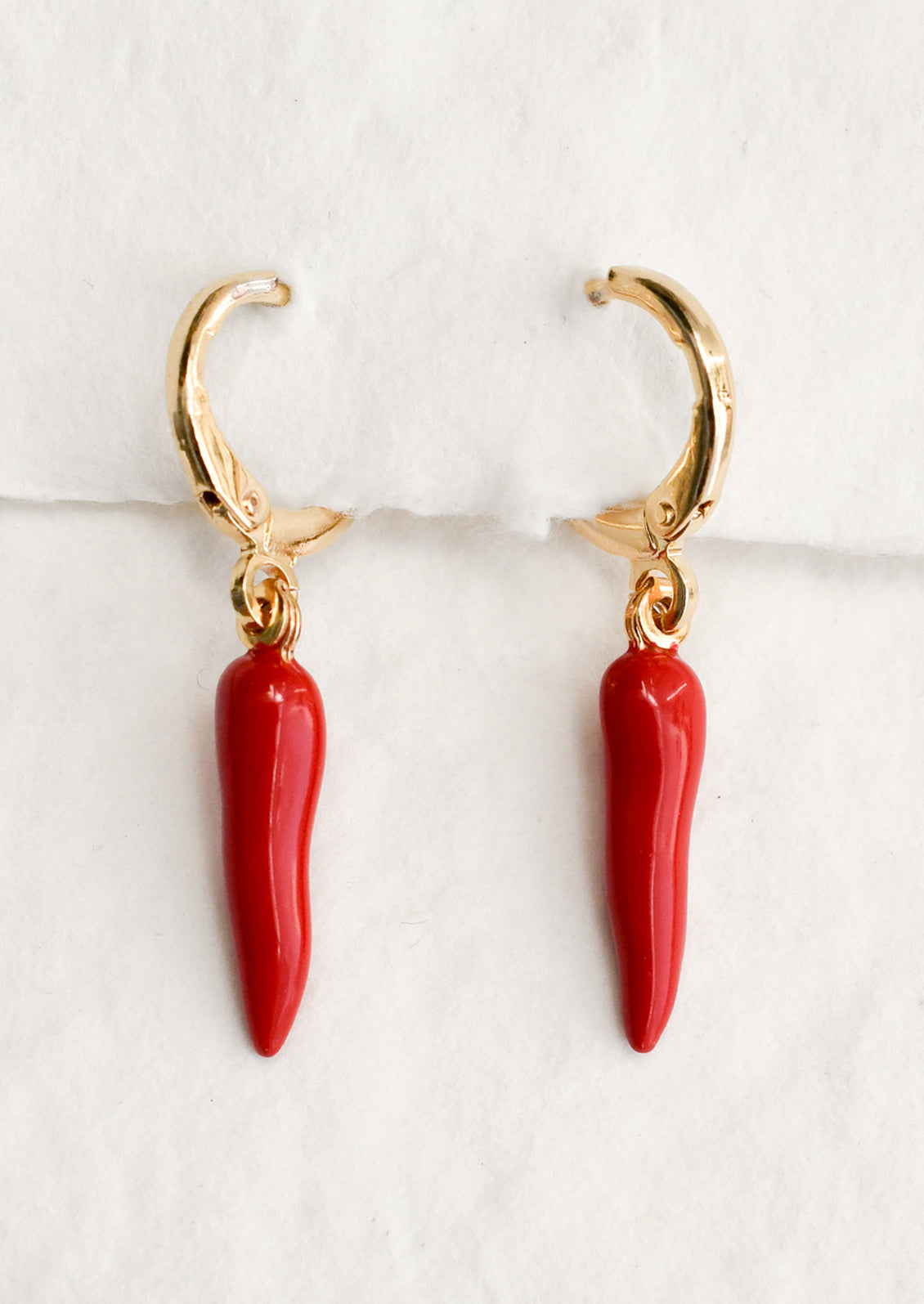 A pair of gold huggie hoop earrings with red pepper charm.