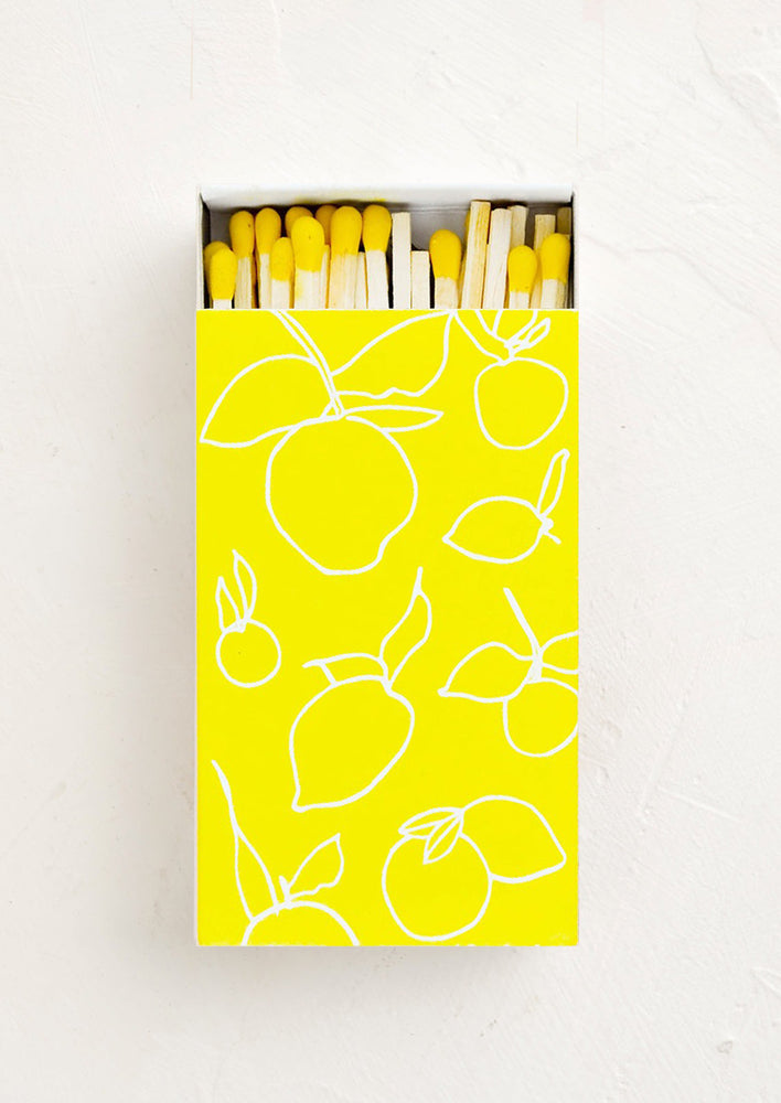 1: A bright yellow matchbox with white lemon outlines printed on it is slid open to display matches with yellow tips.