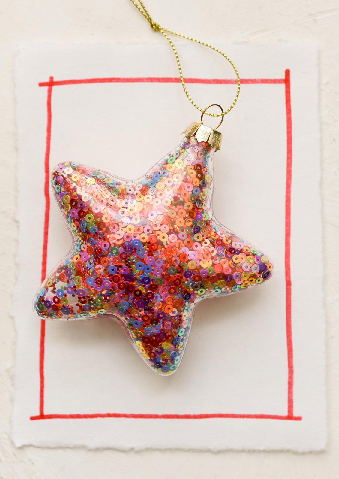 A clear glass star shaped ornament with multicolor sequins inside.