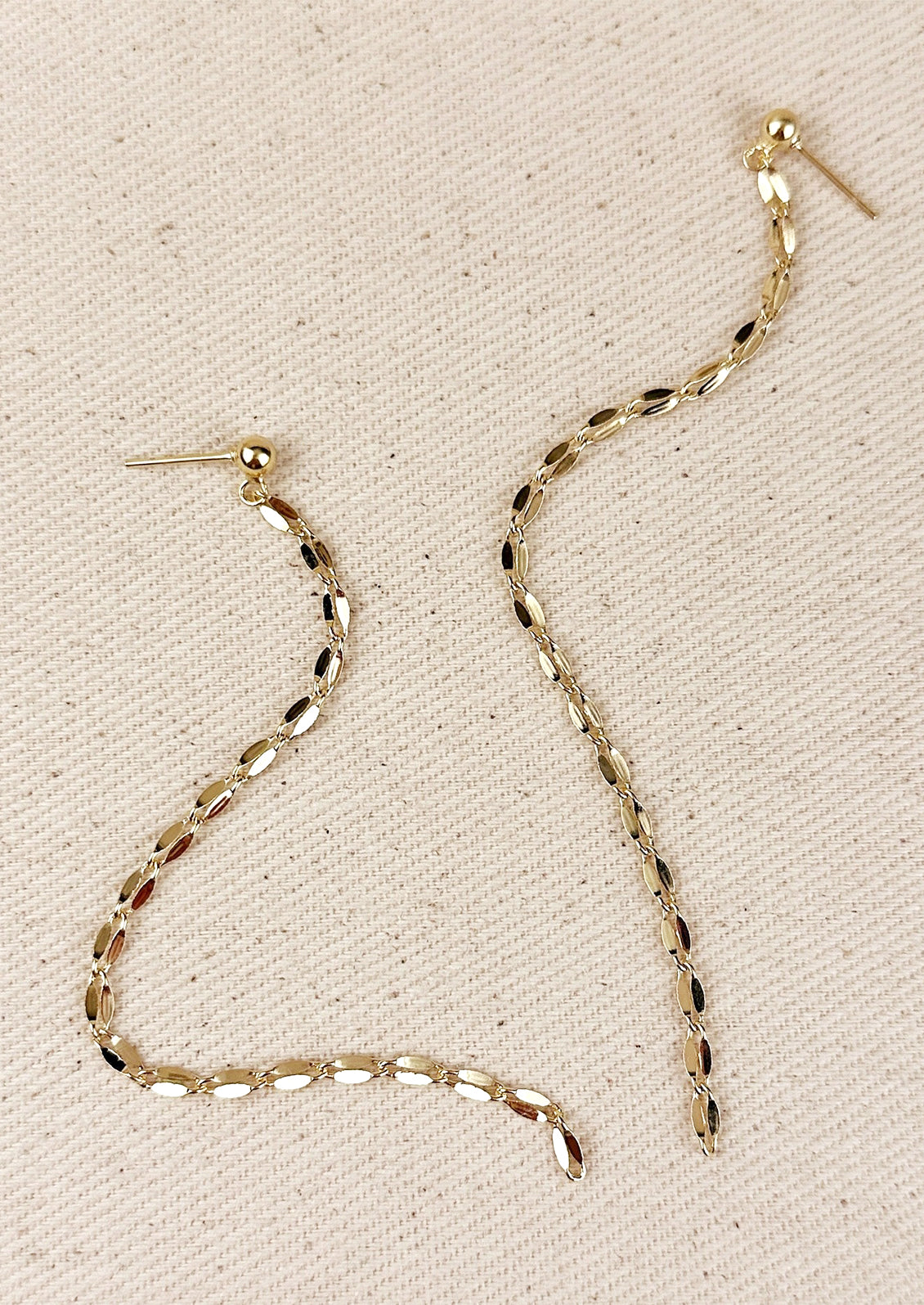 A pair of gold earrings with round ball post and long, dangling gold chain.