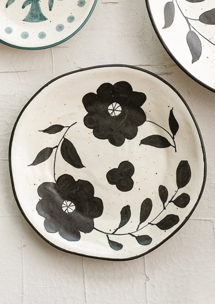 1: A round black and white ceramic platter with large scale black floral pattern.