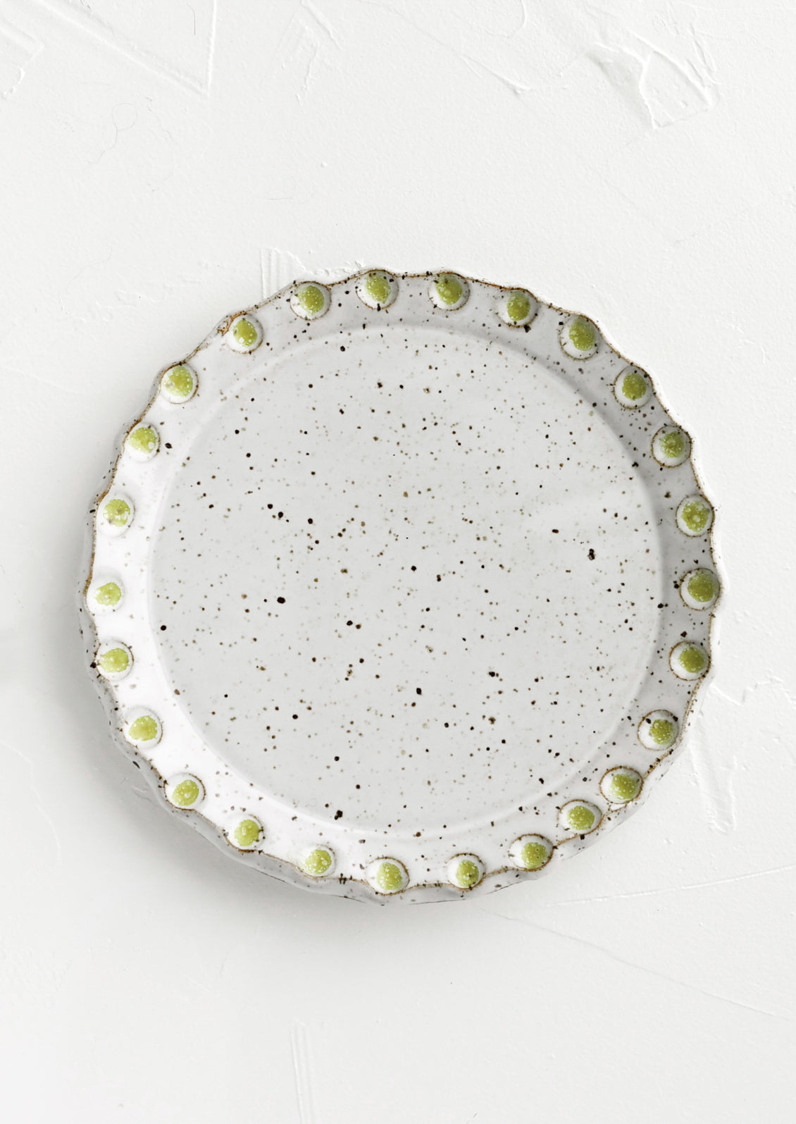 A round ceramic plate with green dot print detail.