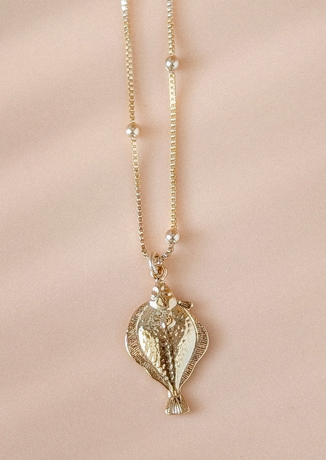 A gold necklace with fish pendant charm.